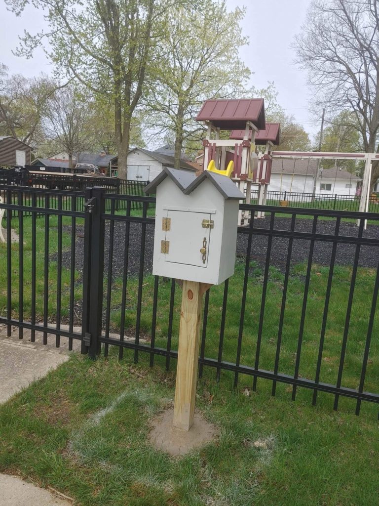 House-shaped Little Free Library mounted on post in front of playground